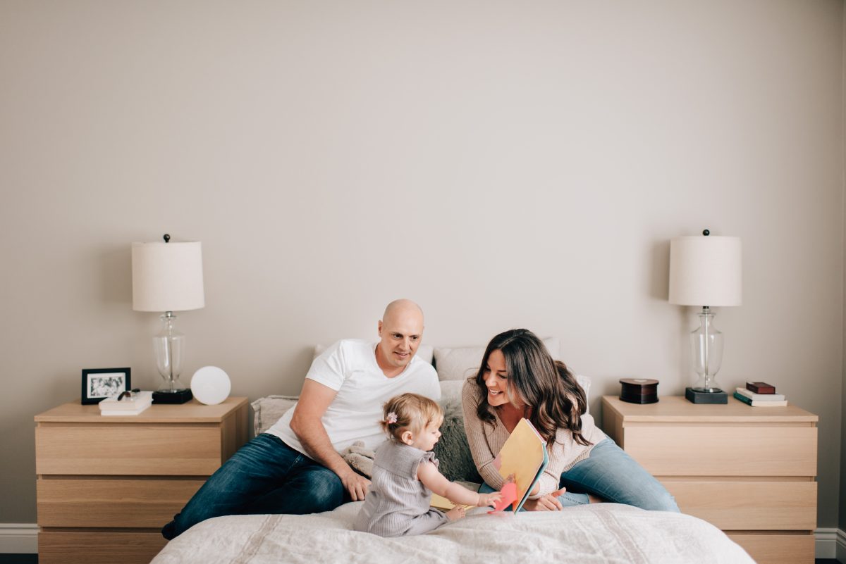 Young parents reading with their toddler on a bed in a minimalist, wellness-focused bedroom designed for better indoor air quality and sleep. bedroom design for wellness