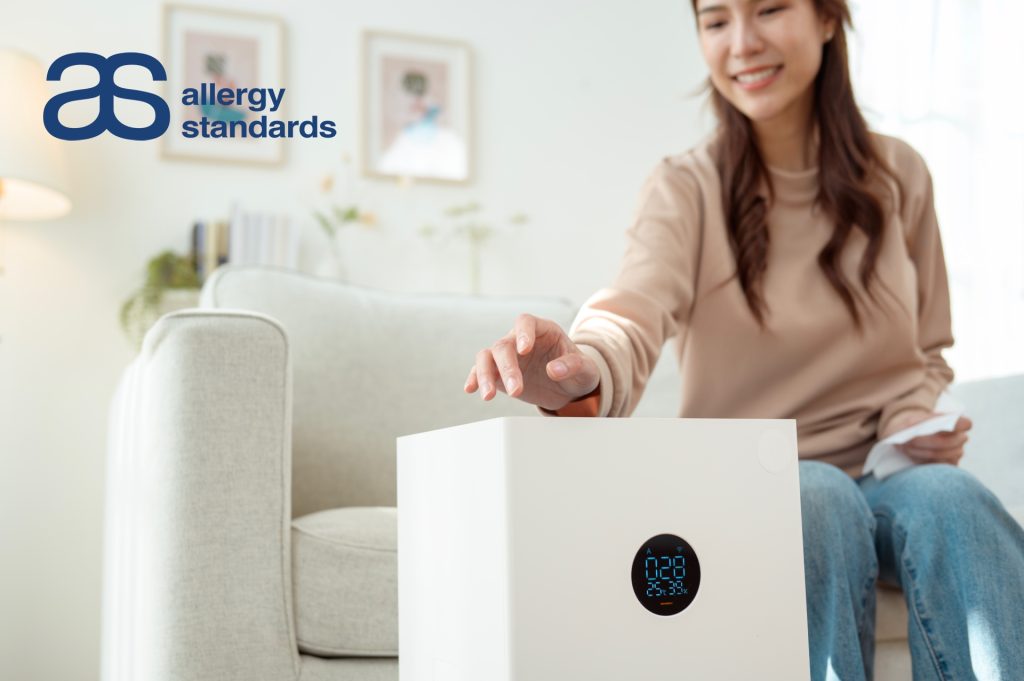 Woman adjusting a compact portable air purifier in a living room, representing Allergy Standards’ expanded certification standard for smaller air cleaning units.