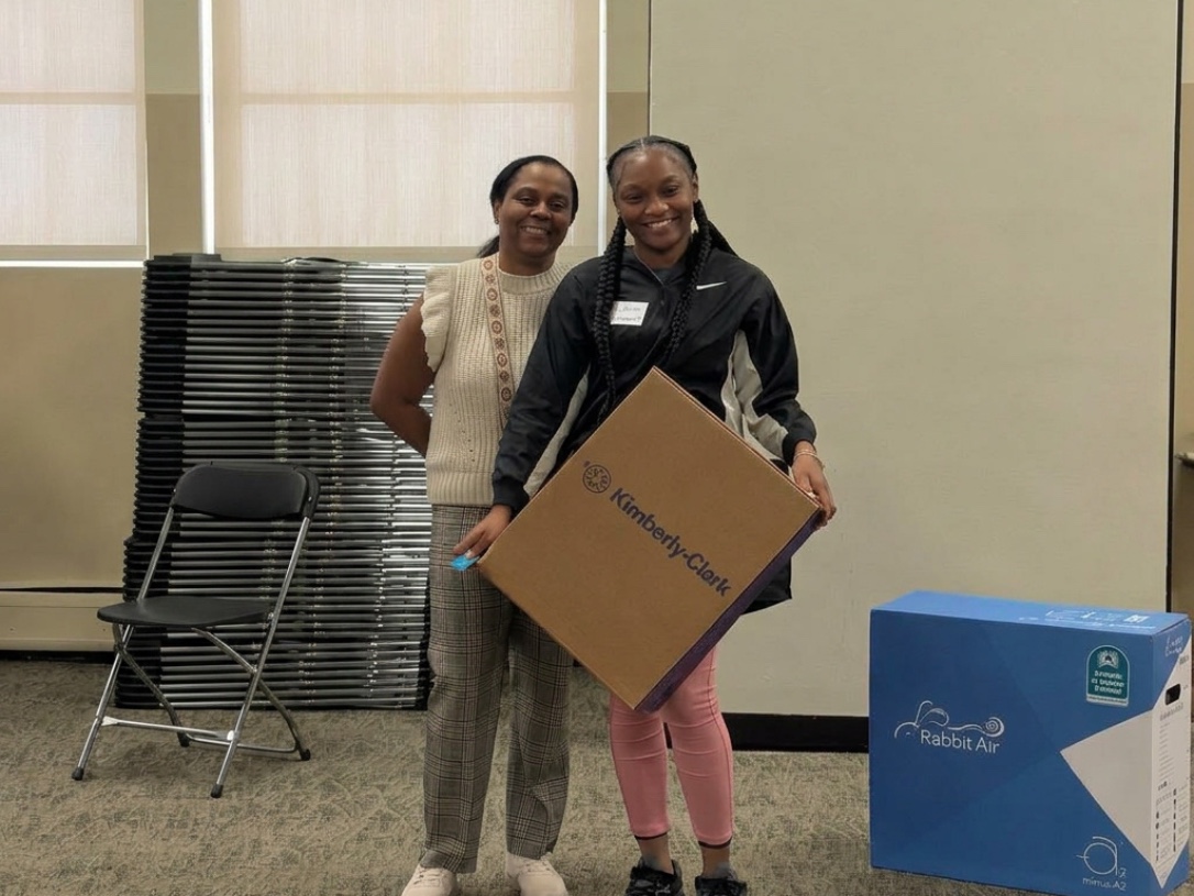 Rachelle Paul-Brutus, Executive Director of the Chicago Asthma Consortium, receiving a Kimberly-Clark Kleenex product donation alongside a Rabbit Air air purifier at the 2026 Community Health Worker Educational Forum, Sinai Chicago.