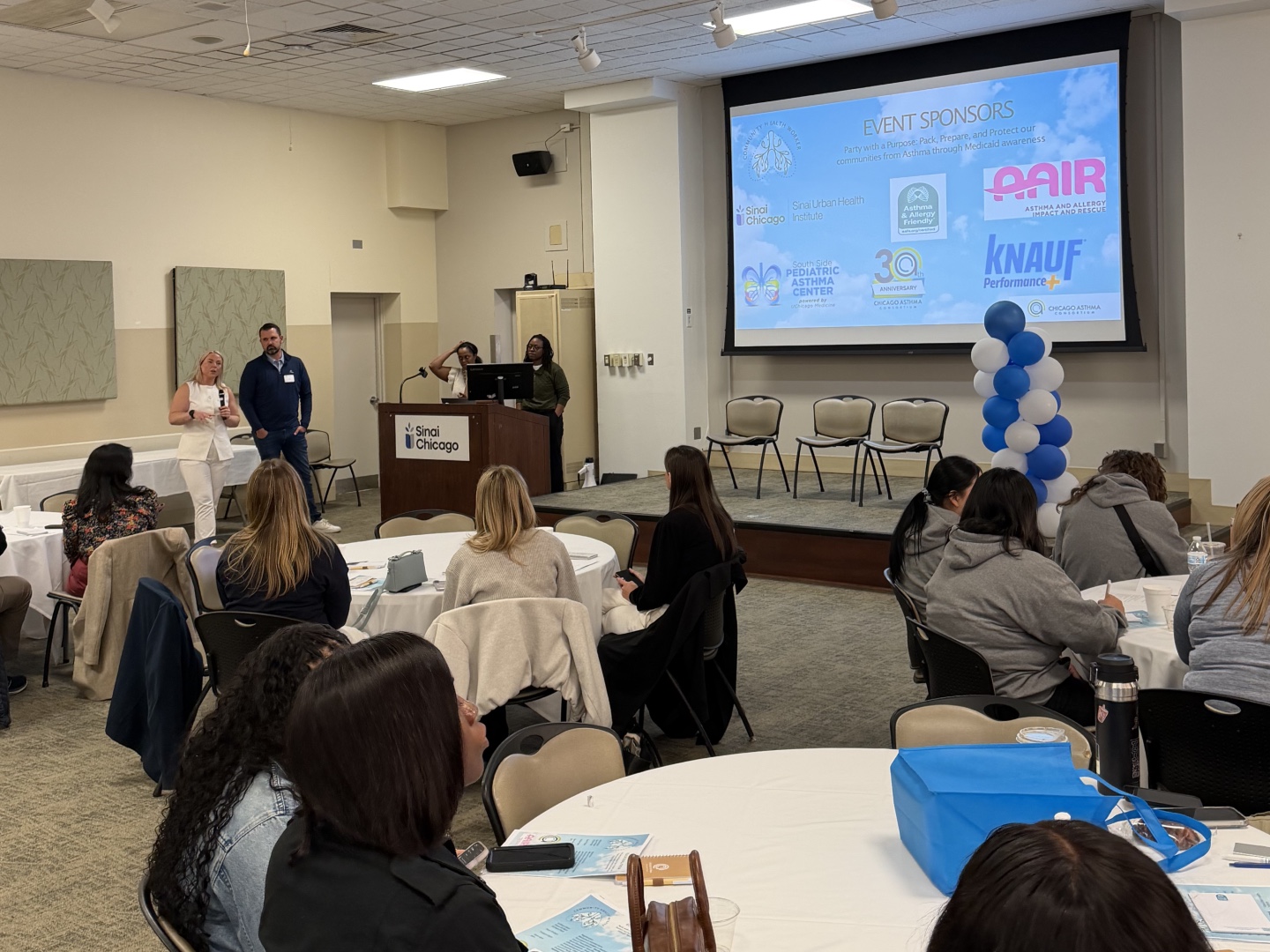 Addressing community health workers at the 2026 Chicago Asthma Consortium Community Health Worker Educational Forum at Sinai Chicago, with event sponsor logos visible on screen.